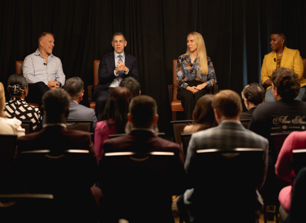 John K. Bates speaking with fellow executives on a panel before a live audience
